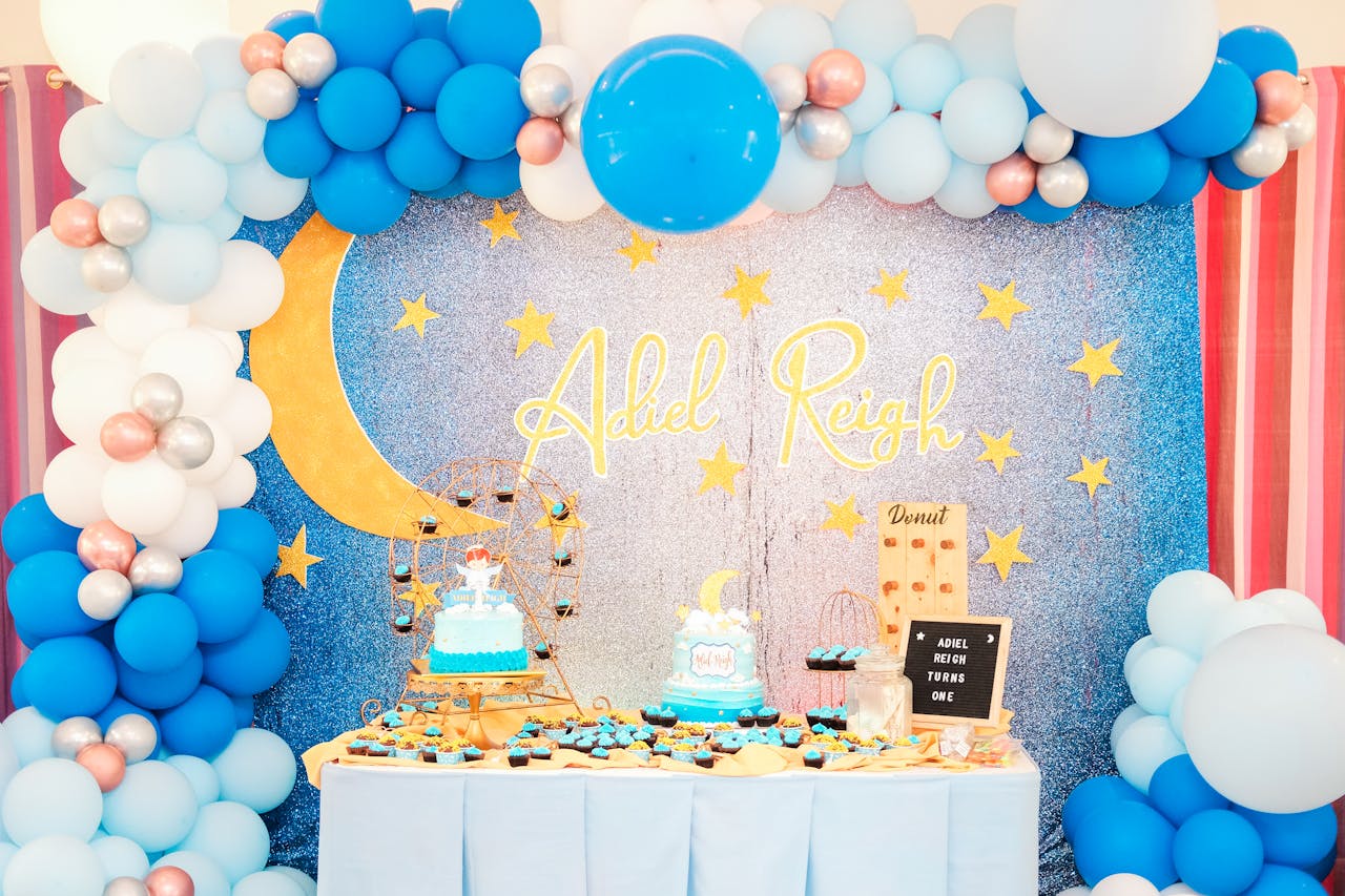 Vibrant moon and star themed baby birthday party decoration with balloons and cake.